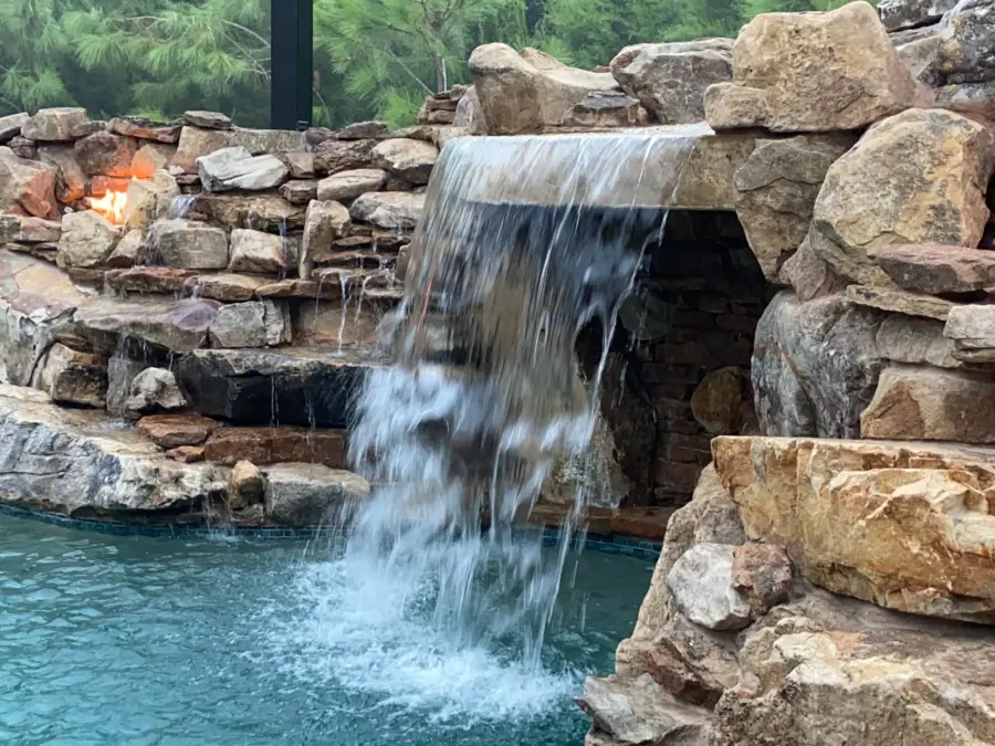 Close view of a boulder grotto waterfall pouring into a pool between two lit fire niches