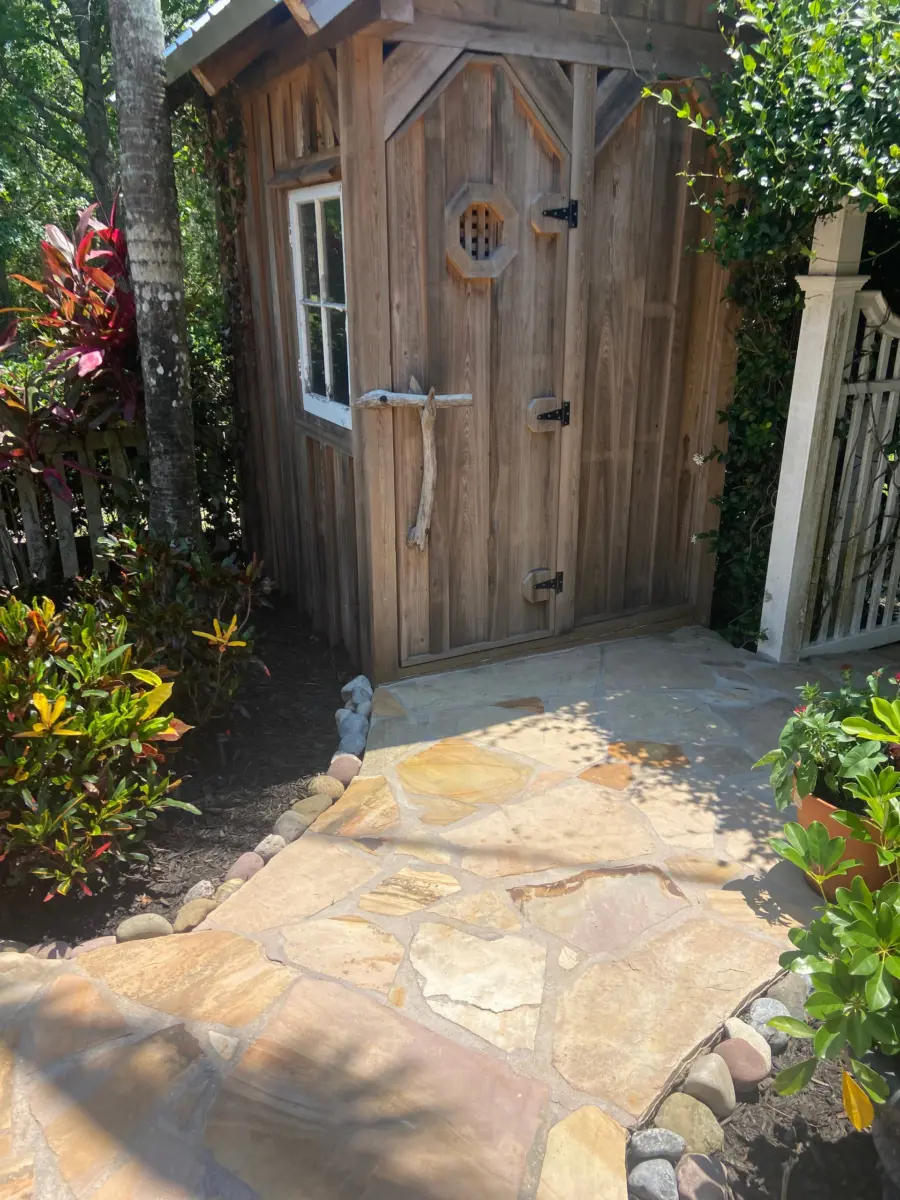 Flagstone path edged with river rock leading to a weathered wood garden shed