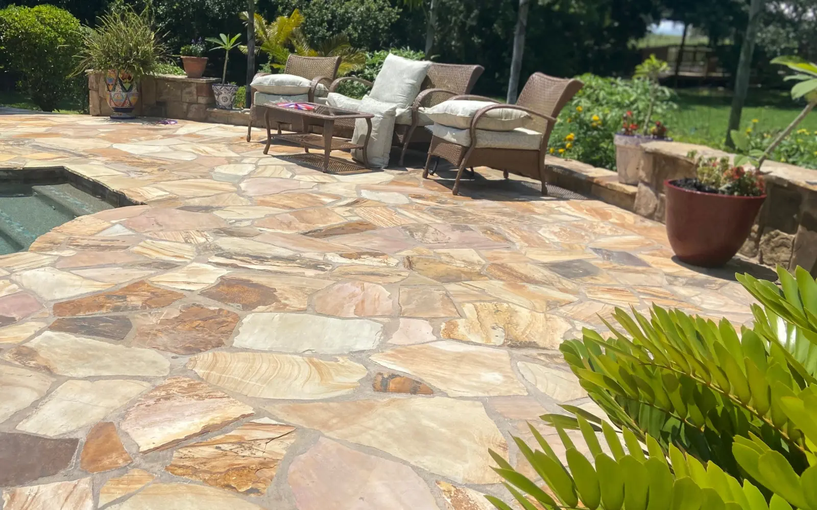 Flagstone patio of warm sandstone in irregular pieces with wicker seating beside a spa