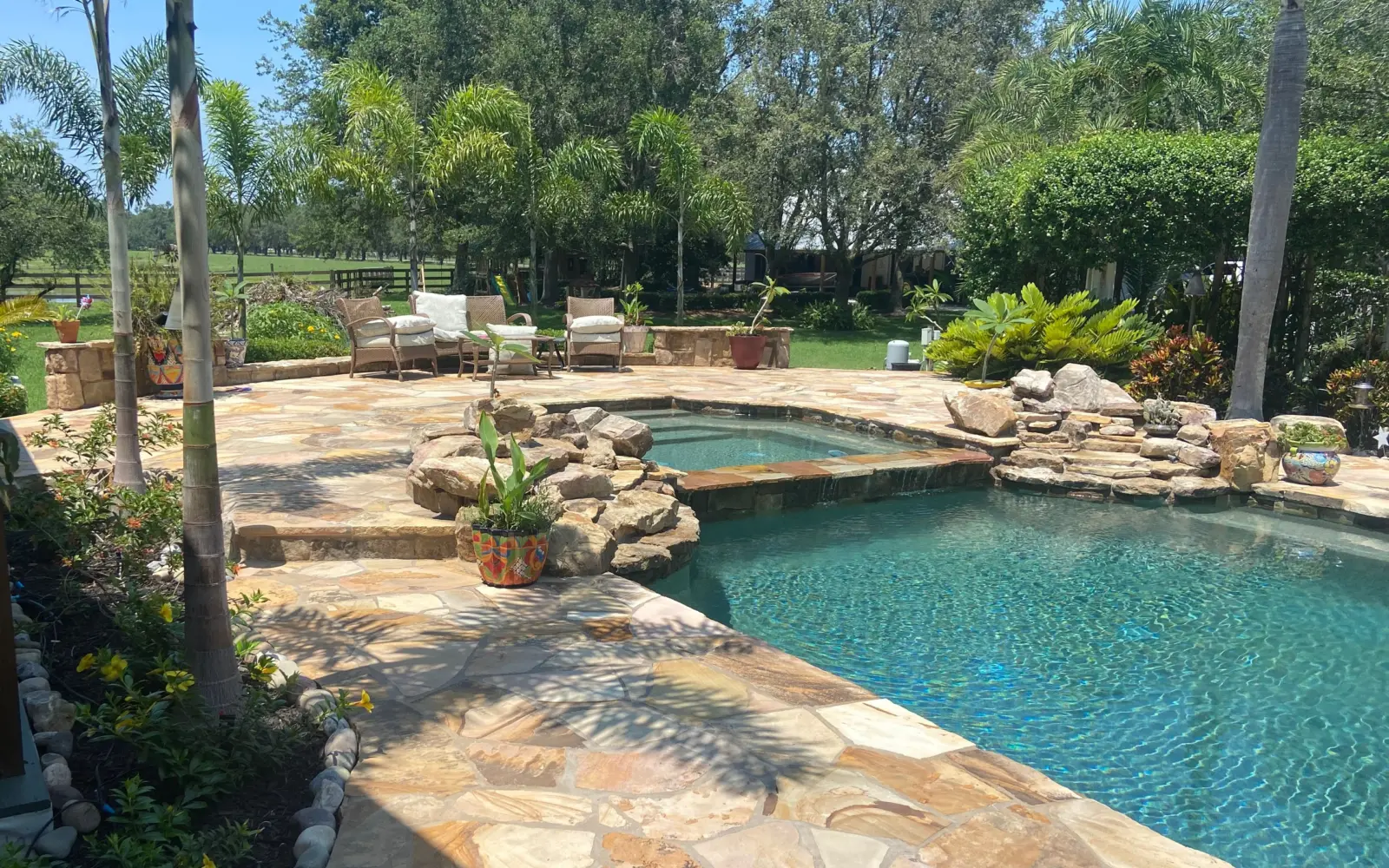 Flagstone pool deck with raised spa spillway, boulder accents, potted plants and palms