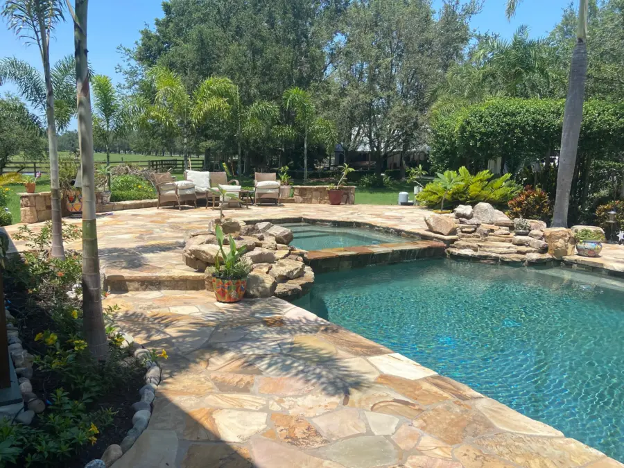 Flagstone pool deck with raised spa spillway, boulder accents, potted plants and palms