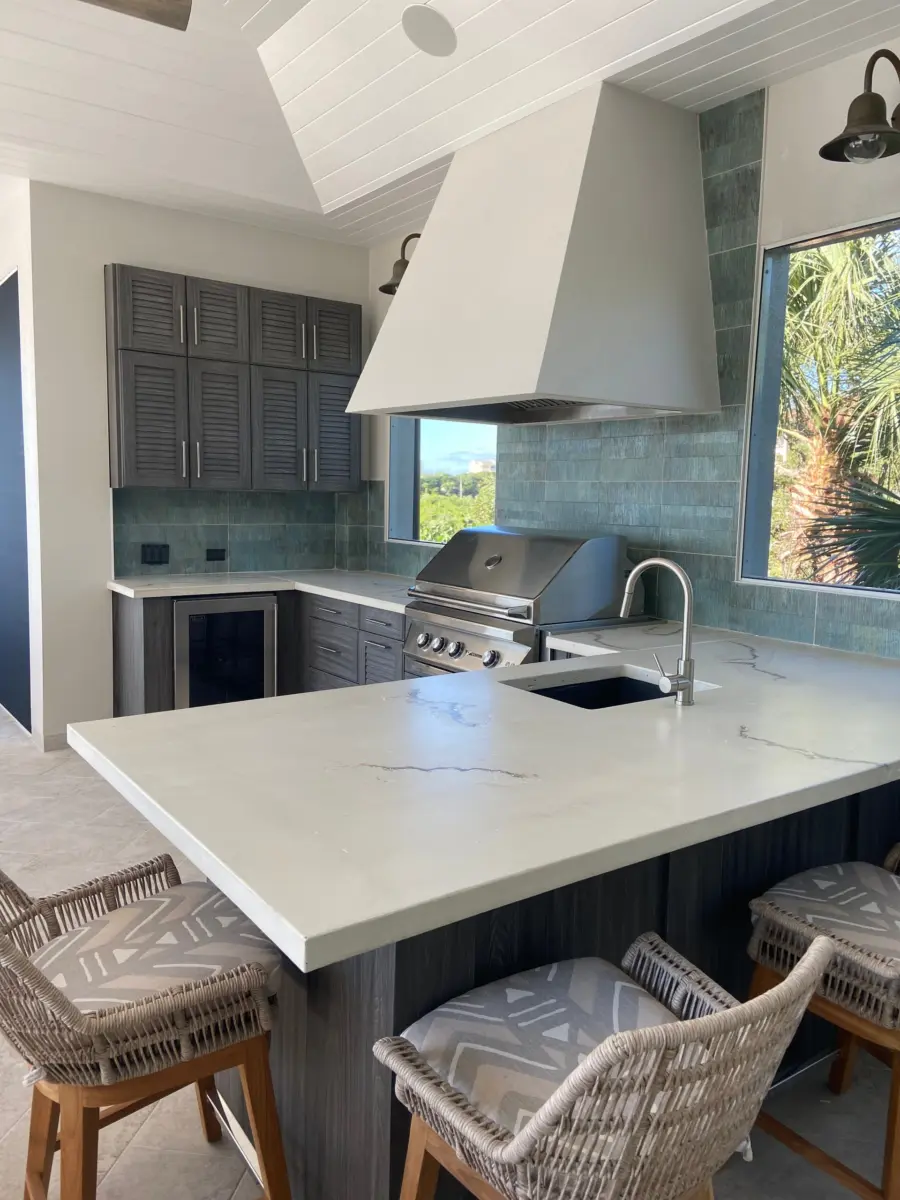 Lanai kitchen bar with white veined countertop, plaster hood, gray cabinets and woven bar stools
