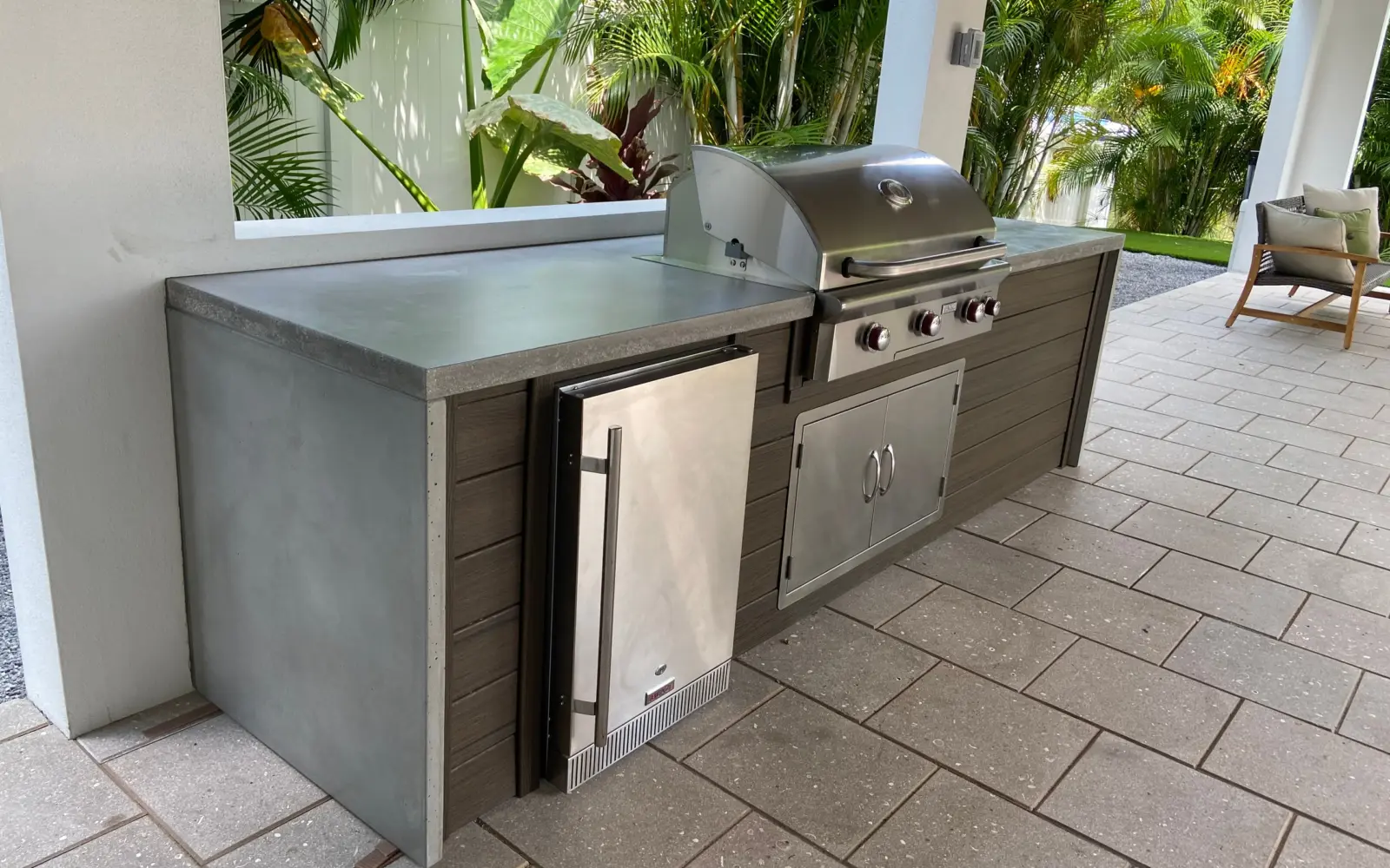 Lanai kitchen with gray concrete countertop and waterfall end, dark wood-look panels and stainless grill