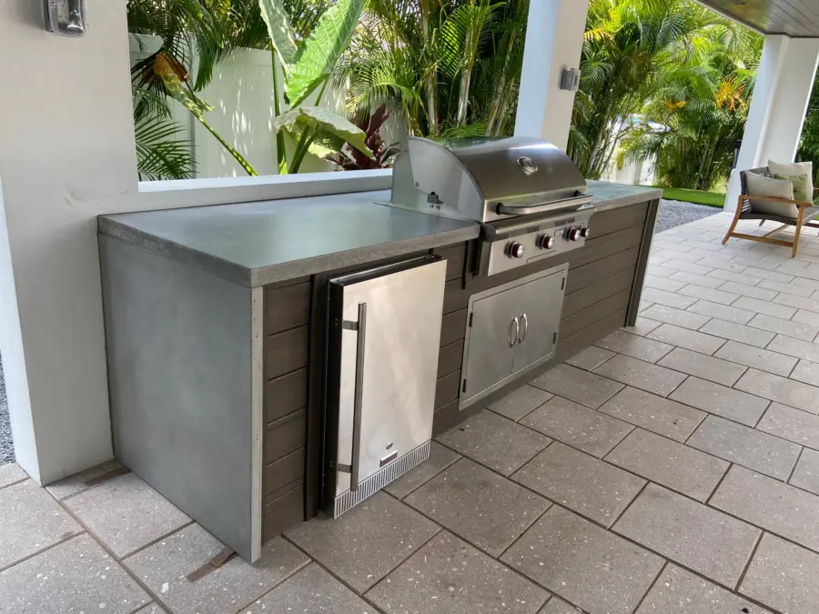 Lanai kitchen with gray concrete countertop and waterfall end, dark wood-look panels and stainless grill