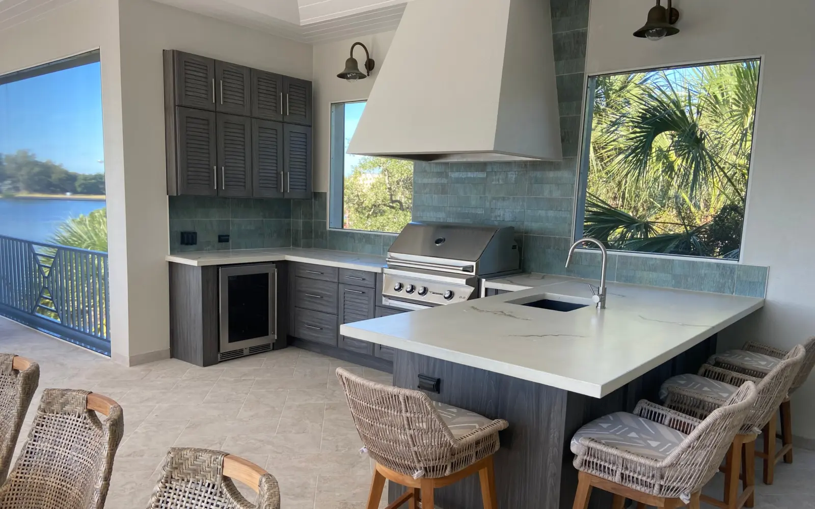 Outdoor kitchen on a lanai with gray louvered cabinets, white veined countertop and plaster vent hood