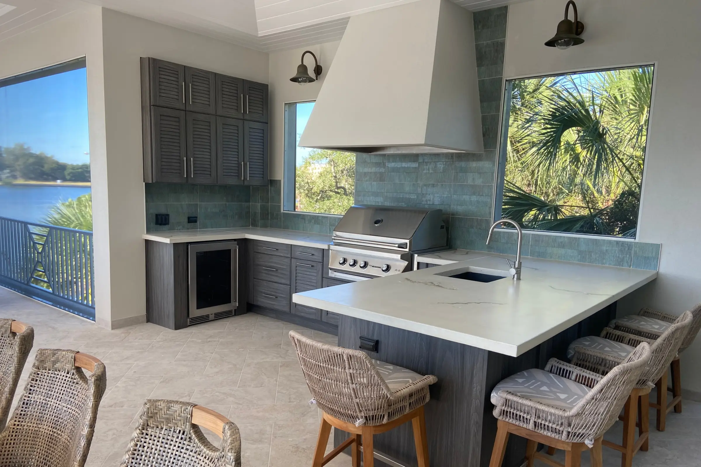 Outdoor kitchen on a lanai with gray louvered cabinets, white veined countertop and plaster vent hood