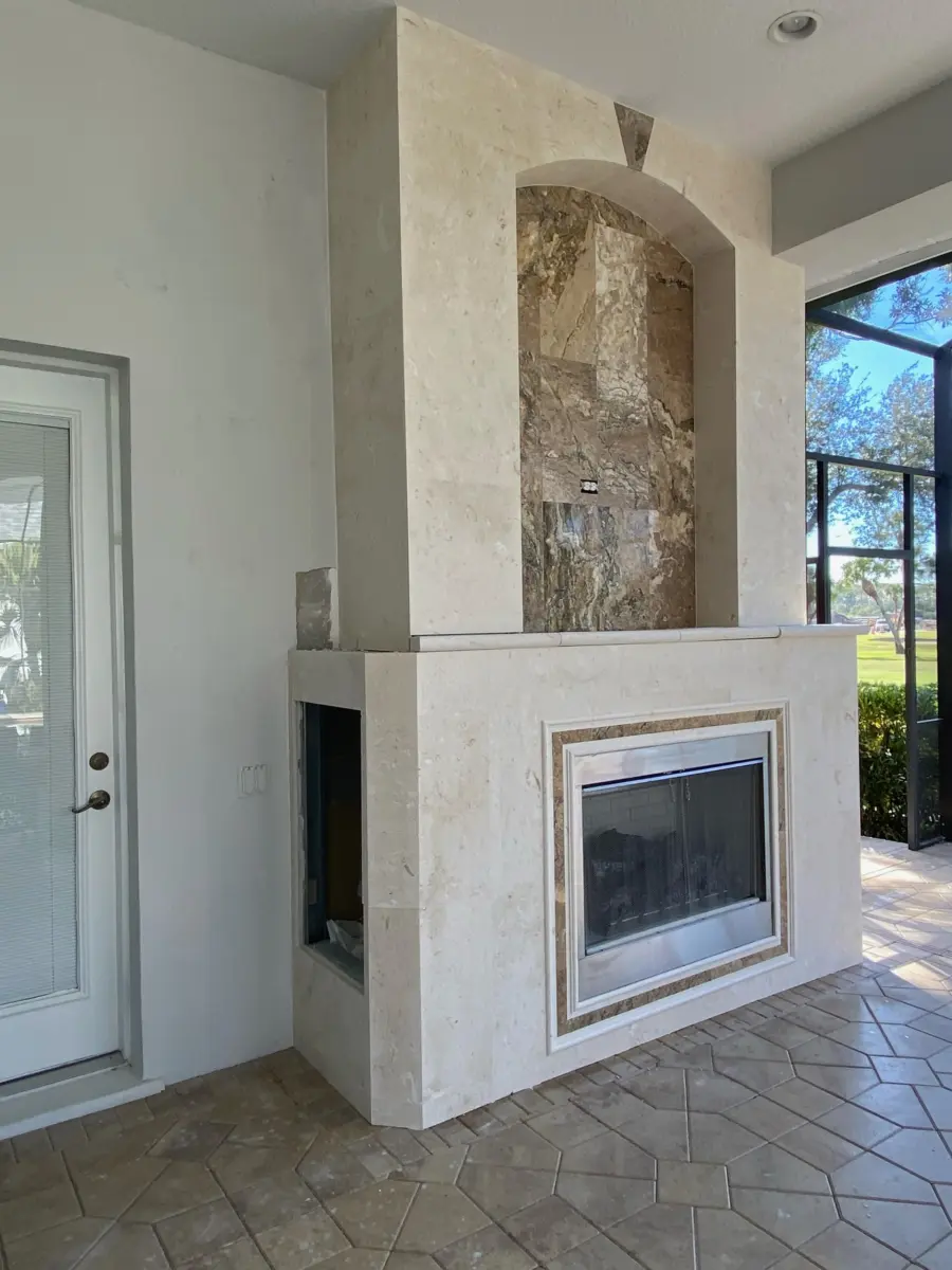 Screened lanai fireplace with cream stone surround, arched stone niche and stainless firebox