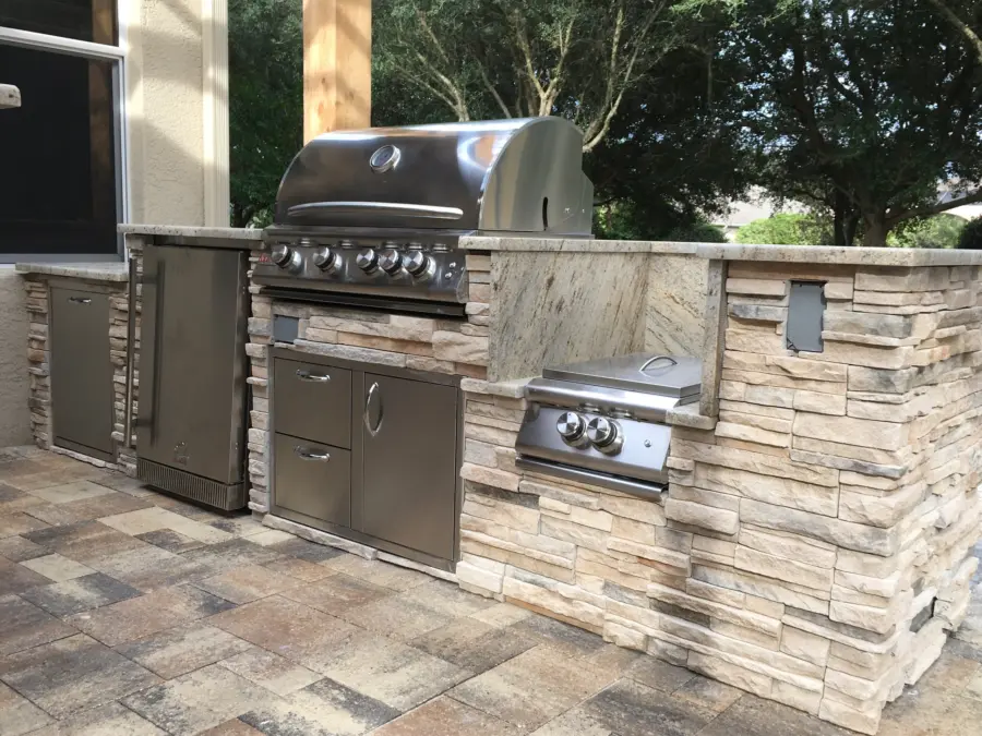 Outdoor kitchen in cream stacked stone with stone countertop, stainless grill, side burner and fridge