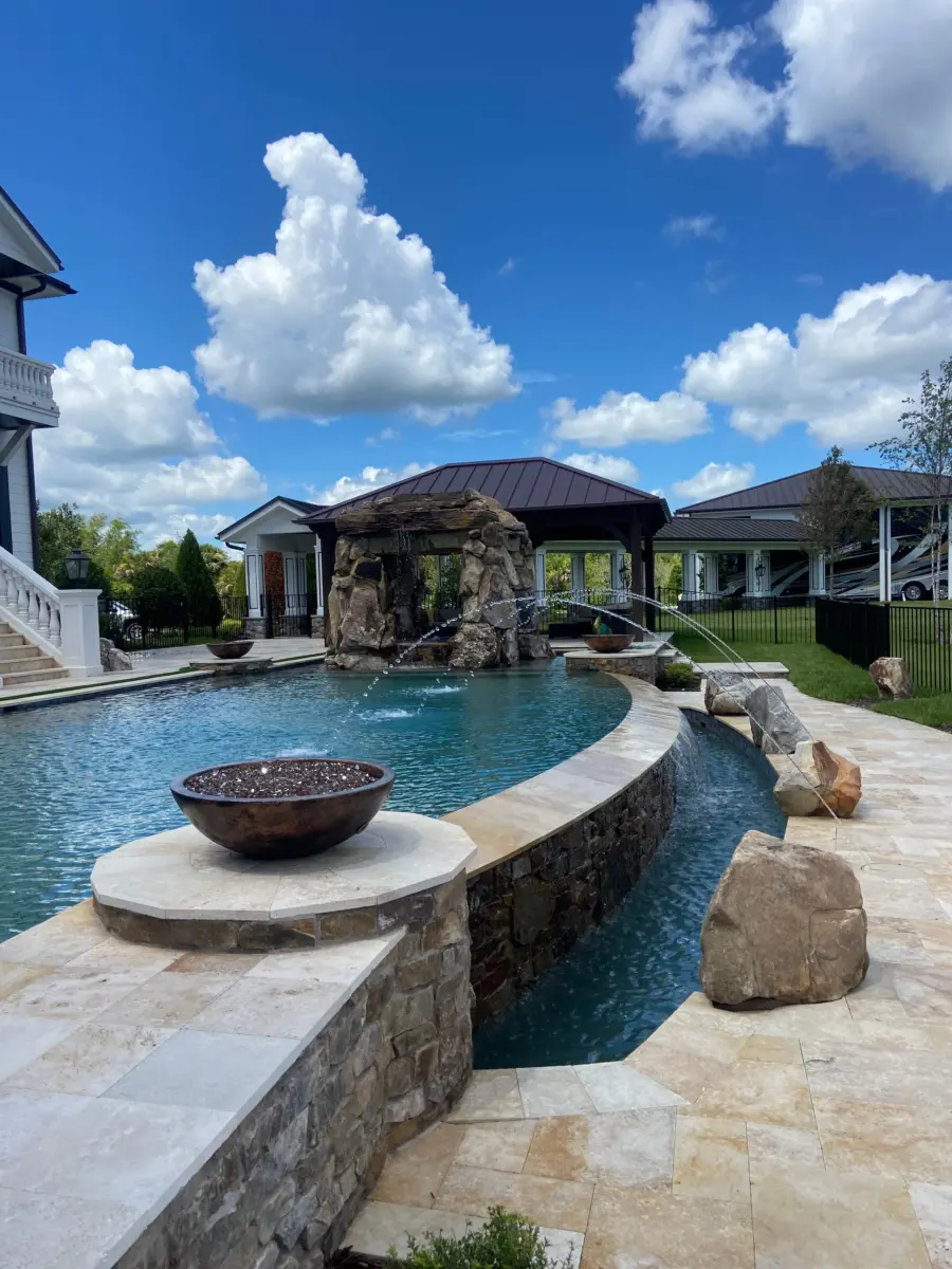 Curved stacked stone pool wall with catch basin, fire bowl on stone pedestal, travertine deck