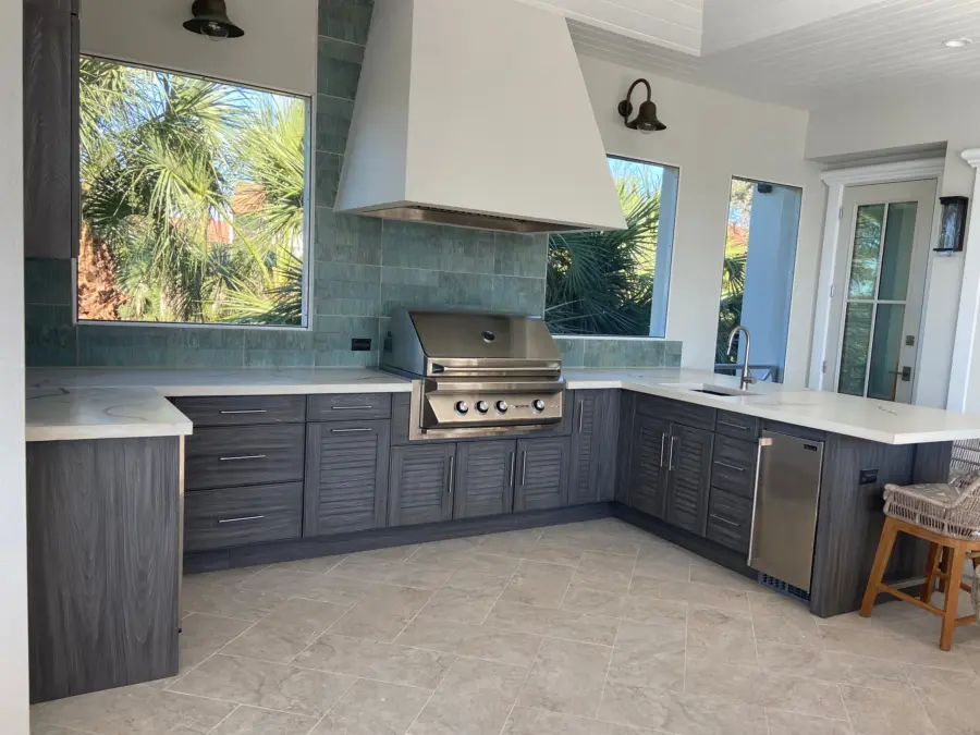 U-shaped outdoor kitchen with gray louvered cabinets, white veined countertops, plaster hood and stainless grill