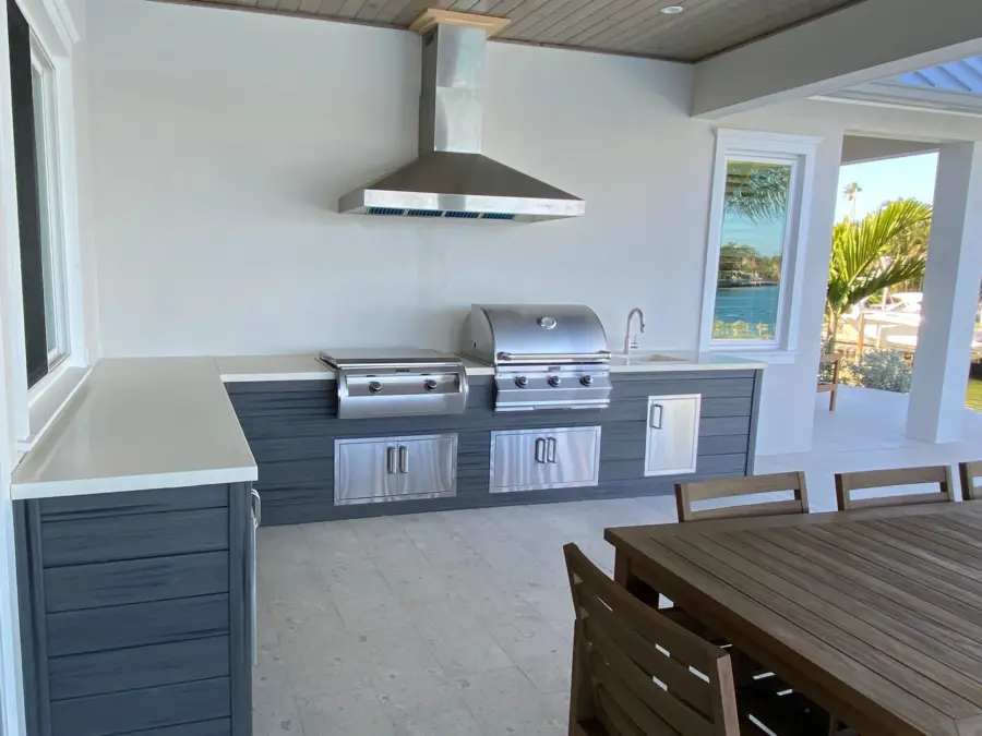 L-shaped lanai kitchen with gray wood-look cabinets, white countertops, stainless grill, griddle and wall hood
