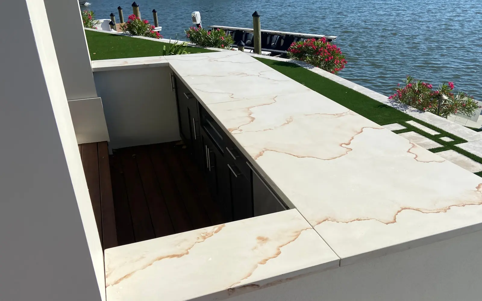 Outdoor bar with white concrete countertops with rust-colored veining beside a canal and dock