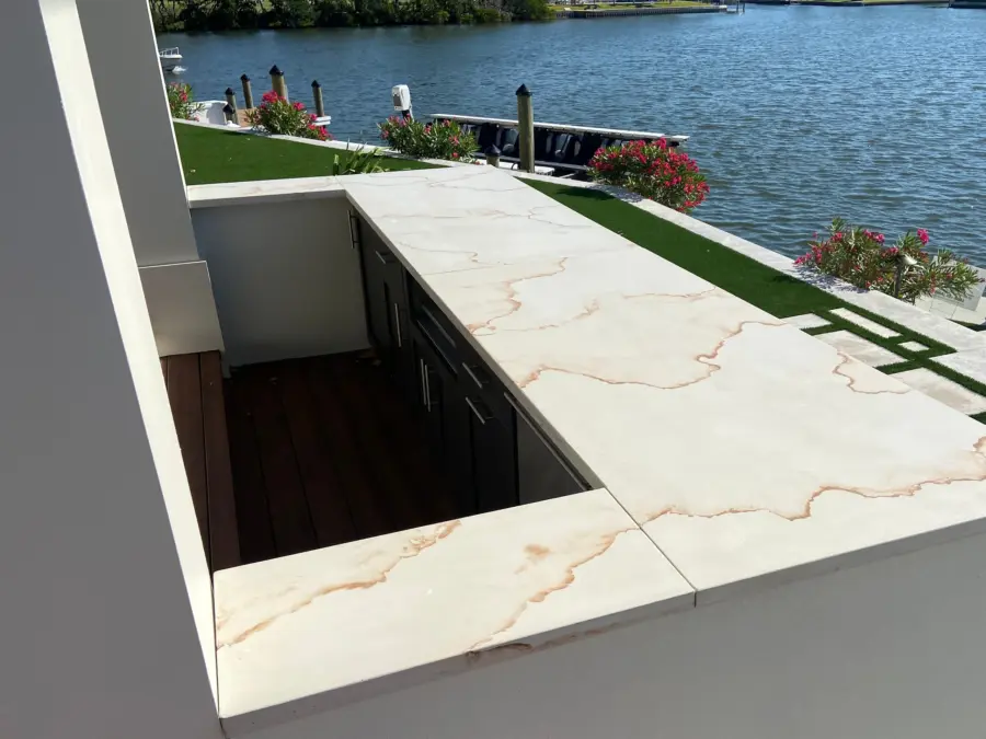 Outdoor bar with white concrete countertops with rust-colored veining beside a canal and dock