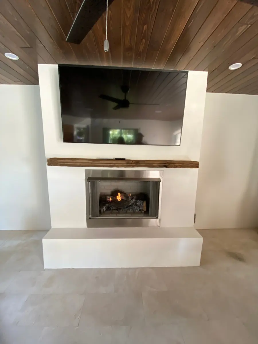 White stucco lanai fireplace with reclaimed wood beam mantel, gas logs and mounted TV
