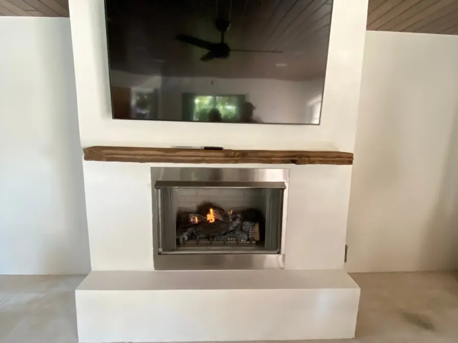 White stucco lanai fireplace with reclaimed wood beam mantel, gas logs and mounted TV